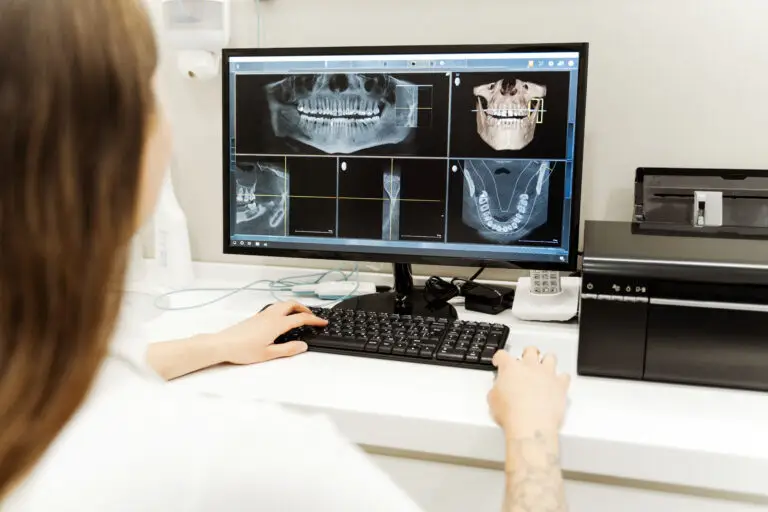 Dentiste ou technicien regardant une radiographie dentaire multi-panneaux sur un écran d'ordinateur dans une clinique.